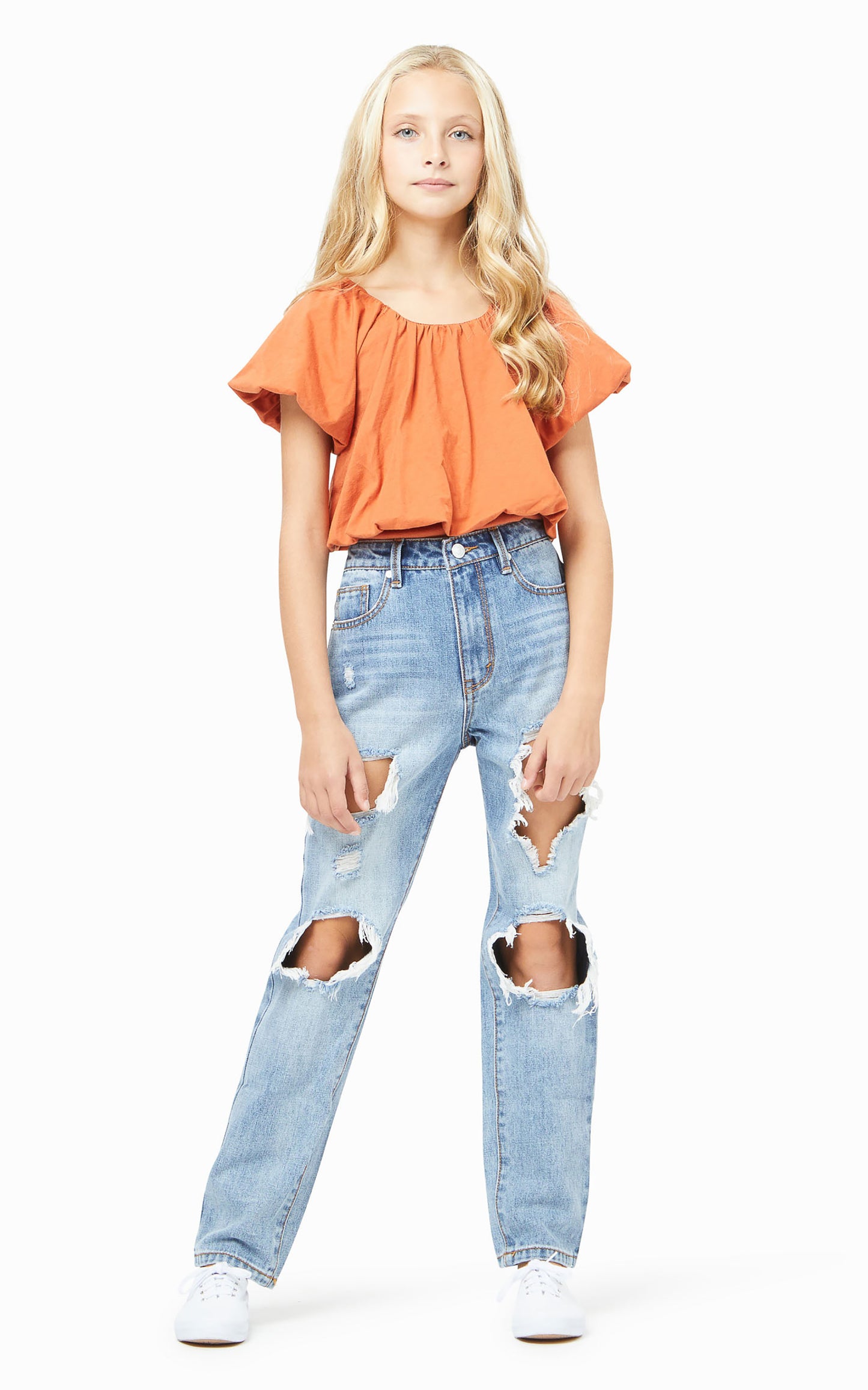 Front view of teen girl wearing an orange off the shoulder top ripped jeans and white shoes 