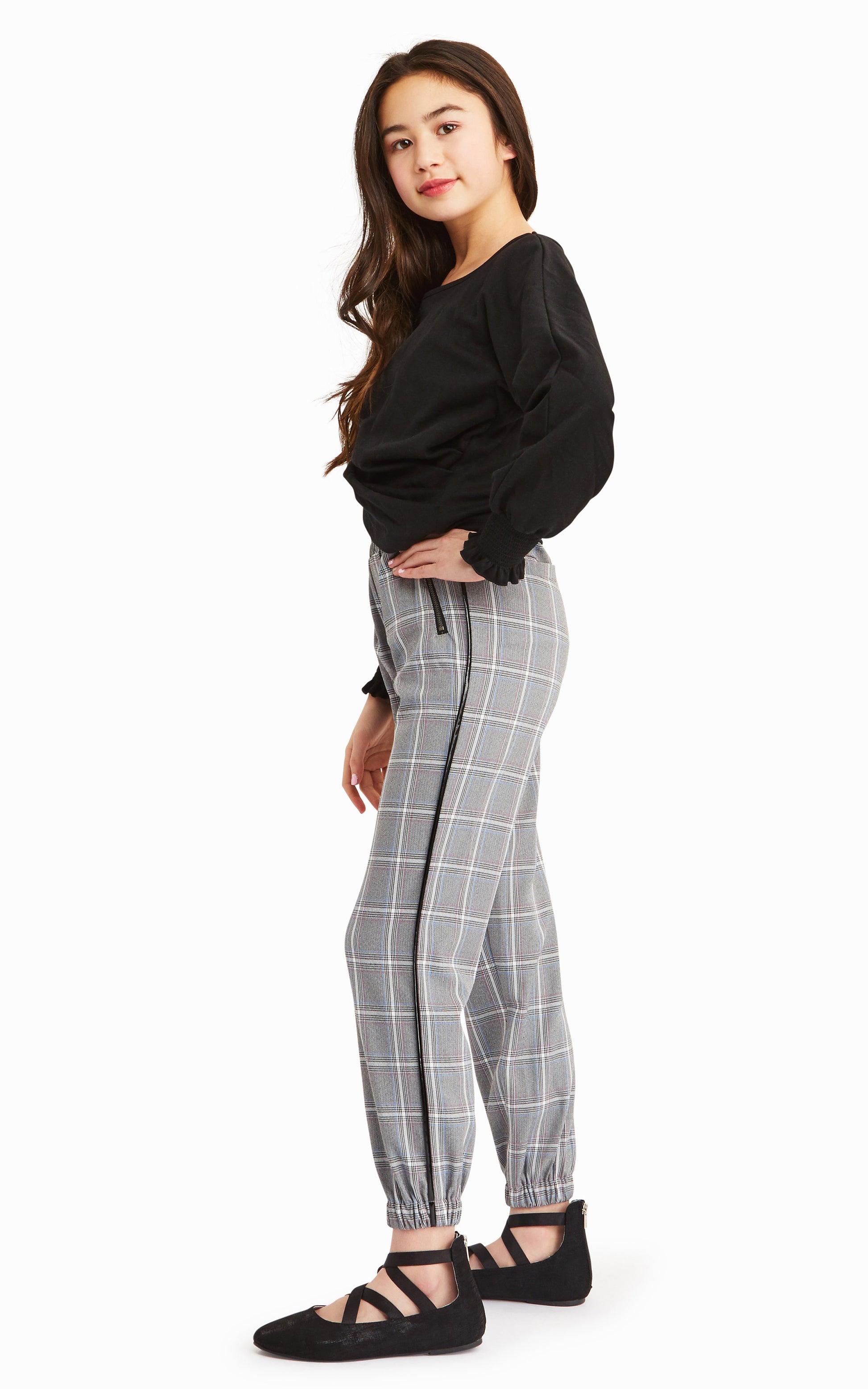 Side view of girl wearing long-sleeve black top with gray, white and black check pattern joggers.