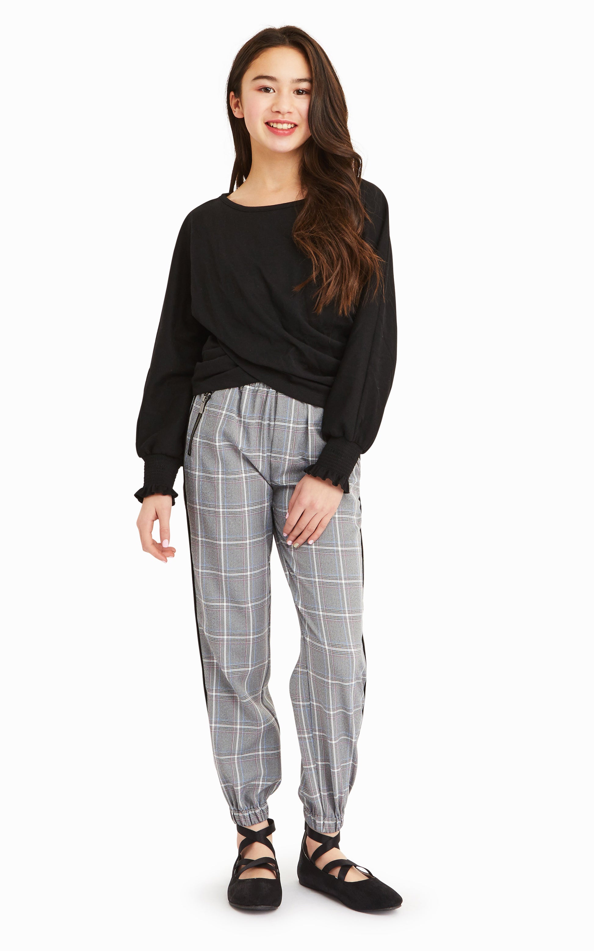 Girl wearing long-sleeve black top with gray, white and black check pattern joggers.