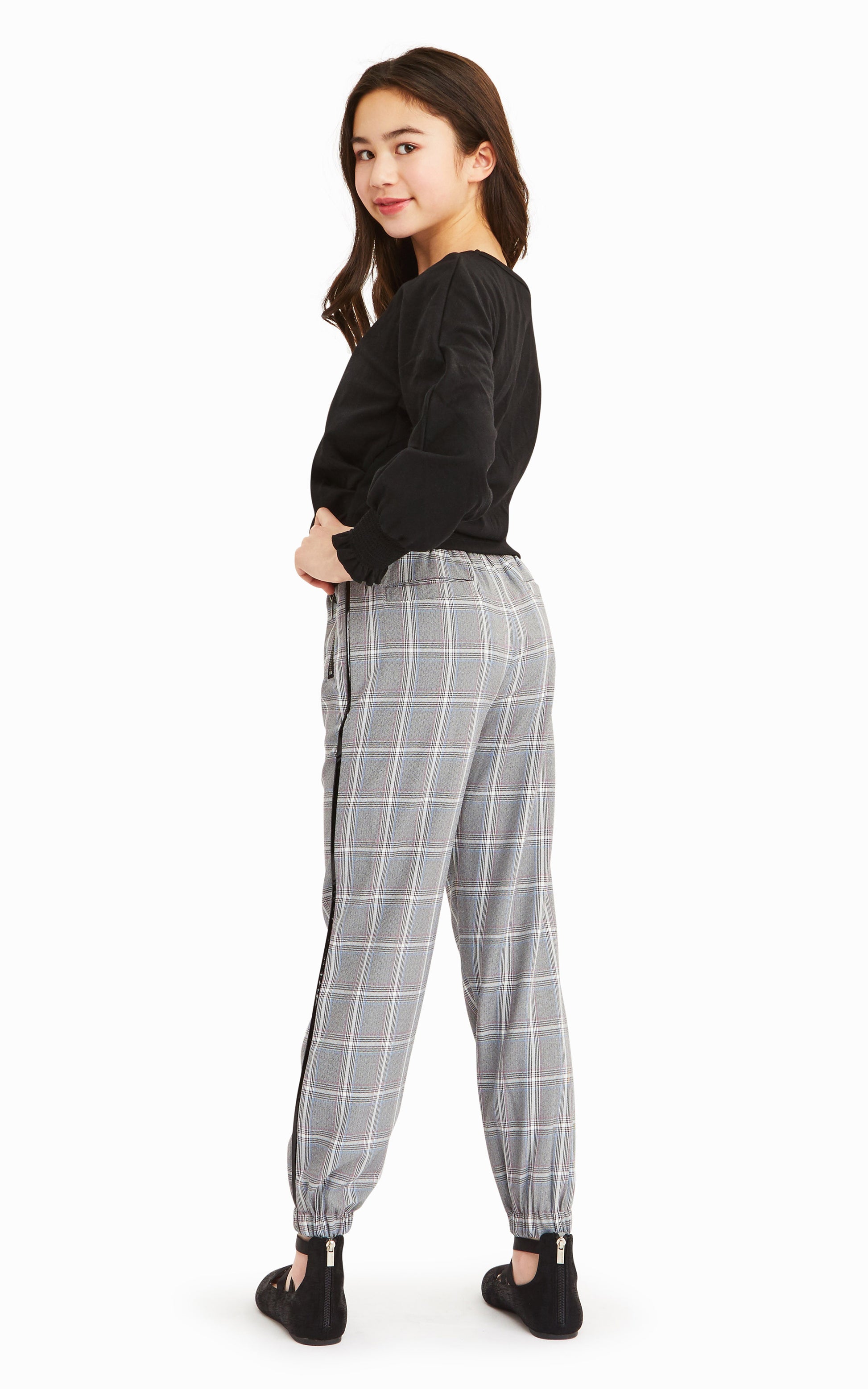 Back view of girl wearing long-sleeve black top with gray, white and black check pattern joggers.