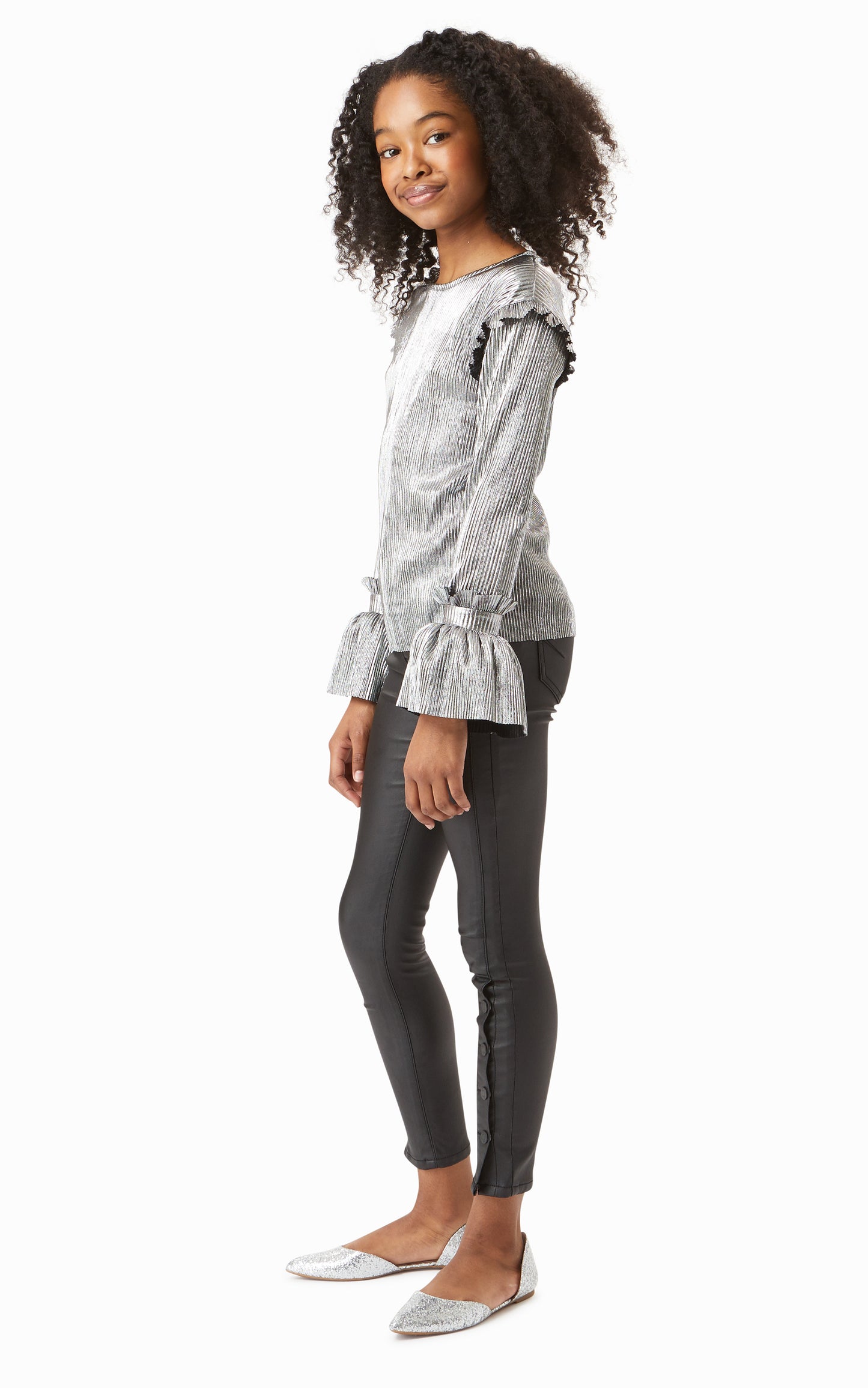 Side view of girl wearing metallic silver long-sleeve top with leather-look skinny jeans. 