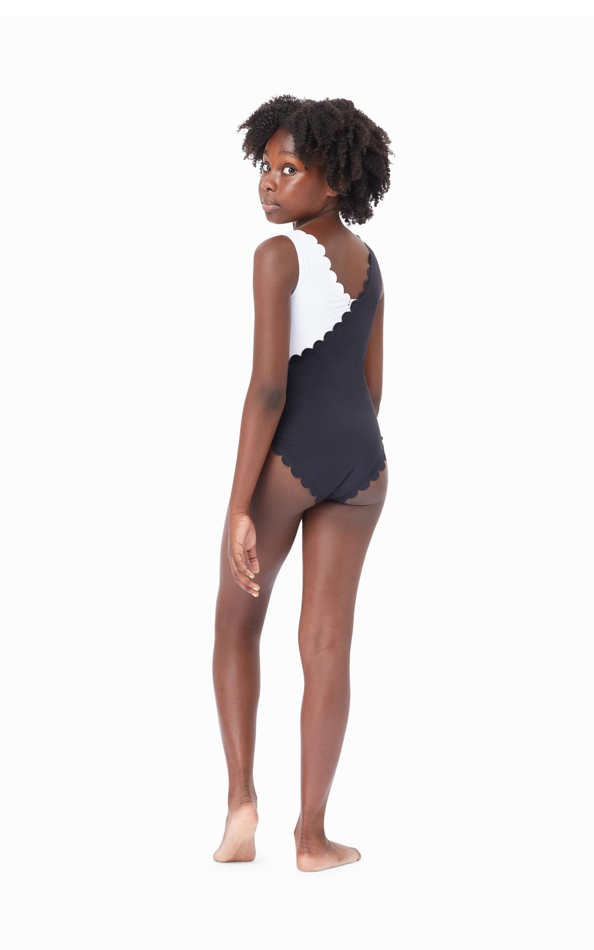 Back of young girl wearing black-and-white color block one-piece swimsuit with scalloped trim