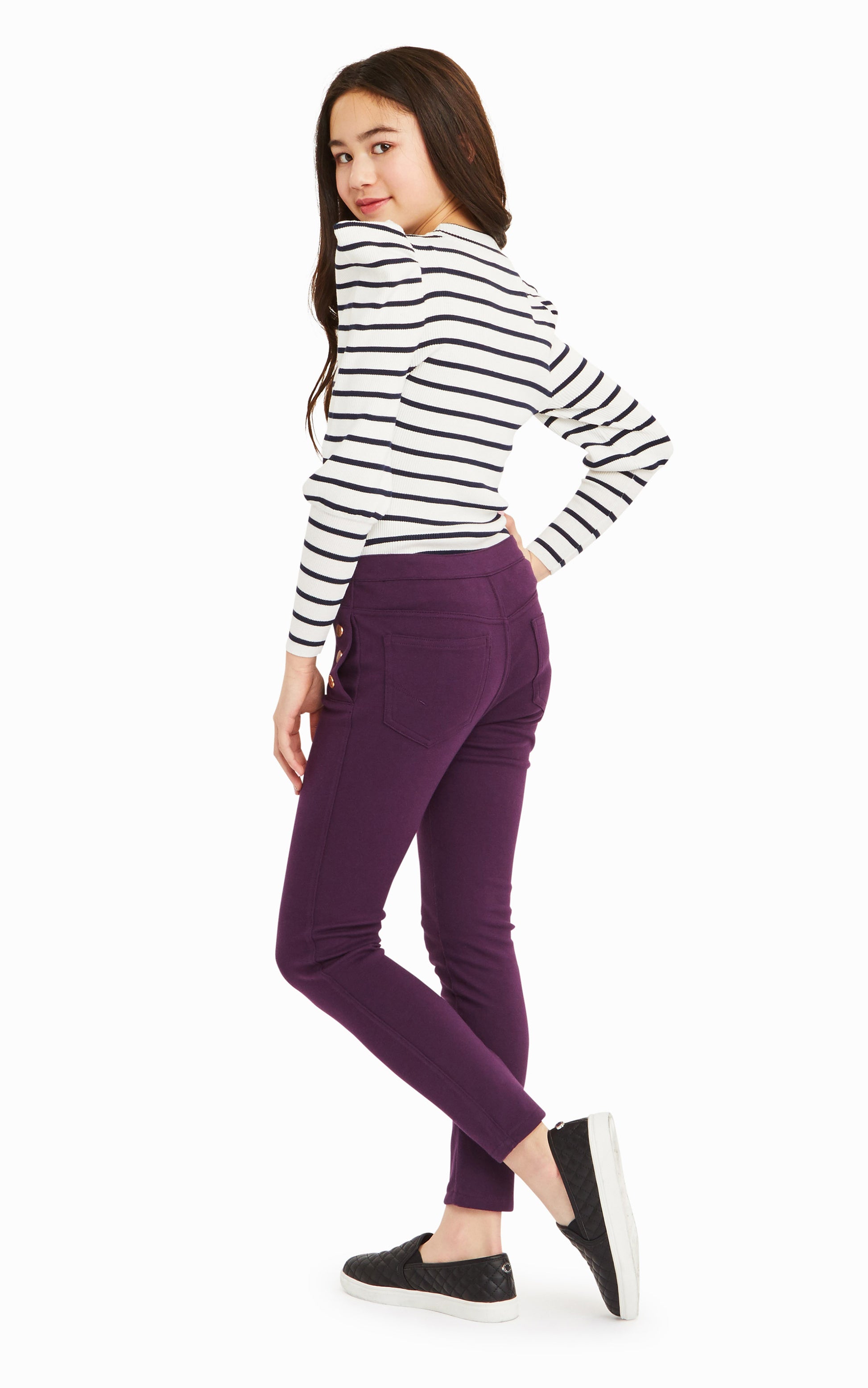 Back view of girl wearing white and black-striped long-sleeve top with purple snap-front pants.