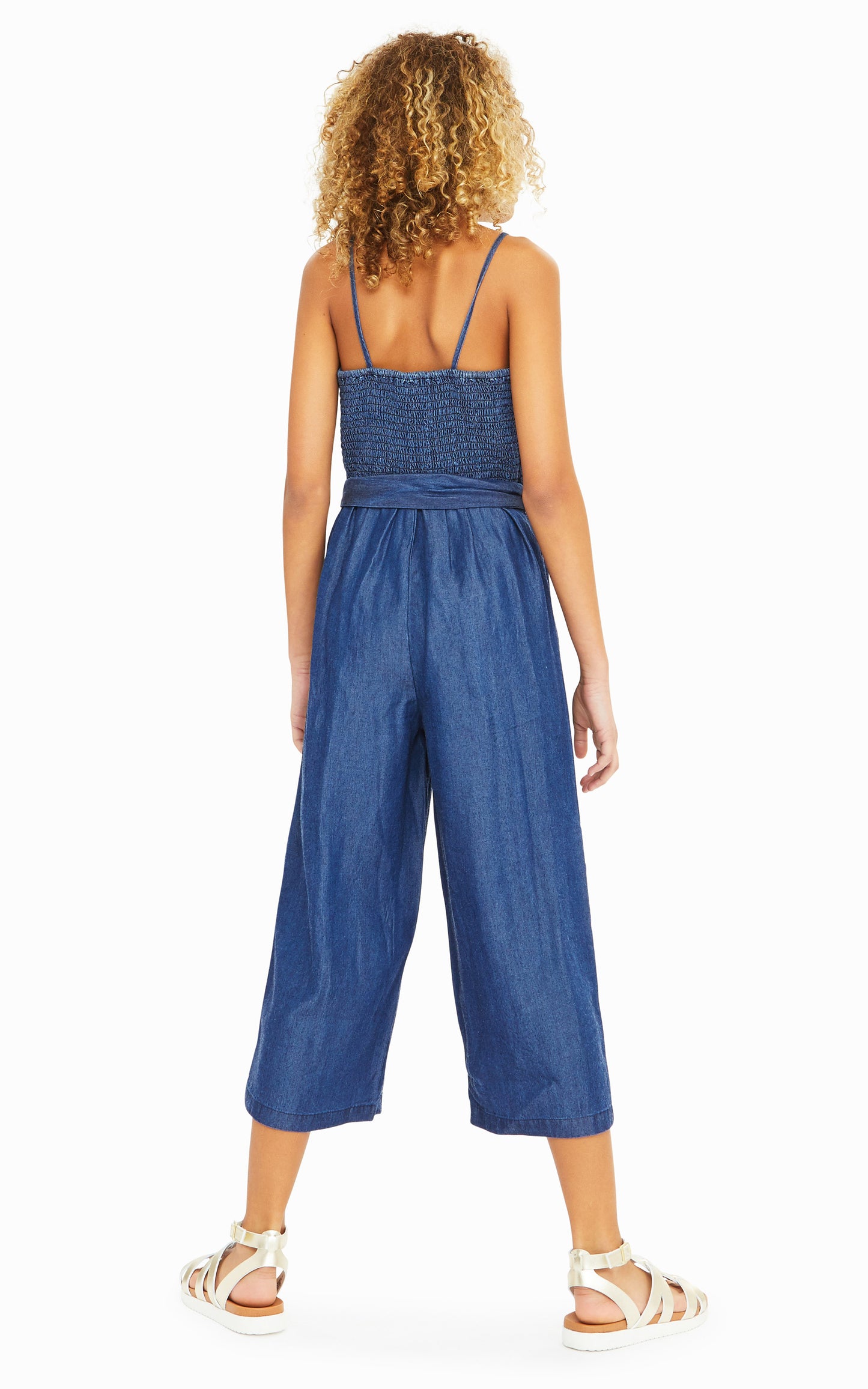 Back view of girl wearing denim-colored sleeveless jumpsuit with belted waist.