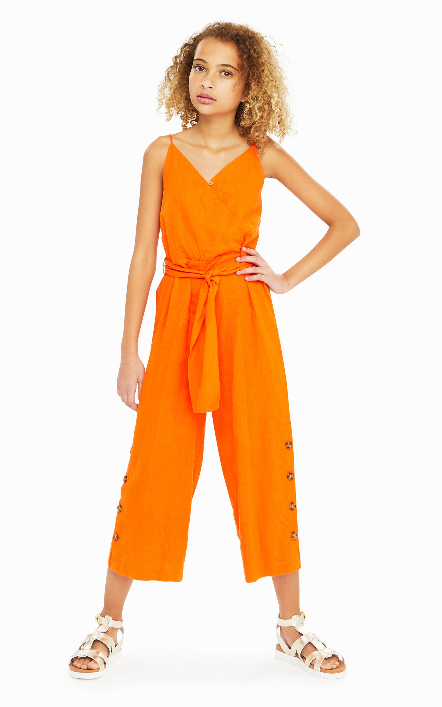 Girl wearing orange sleeveless jumpsuit with belted waist and leopard print button accents on legs.