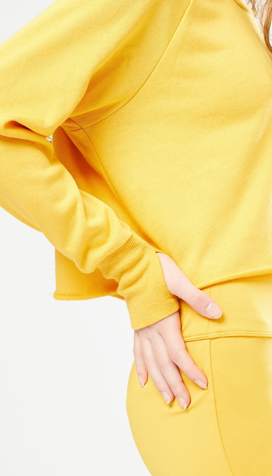 Close up side view of girl wearing yellow long-sleeve top with thumb hole and matching shorts.