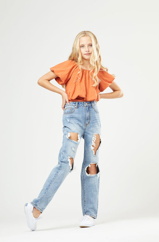 Front view of teen girl wearing an orange off the shoulder top and ripped jeans and white shoes 