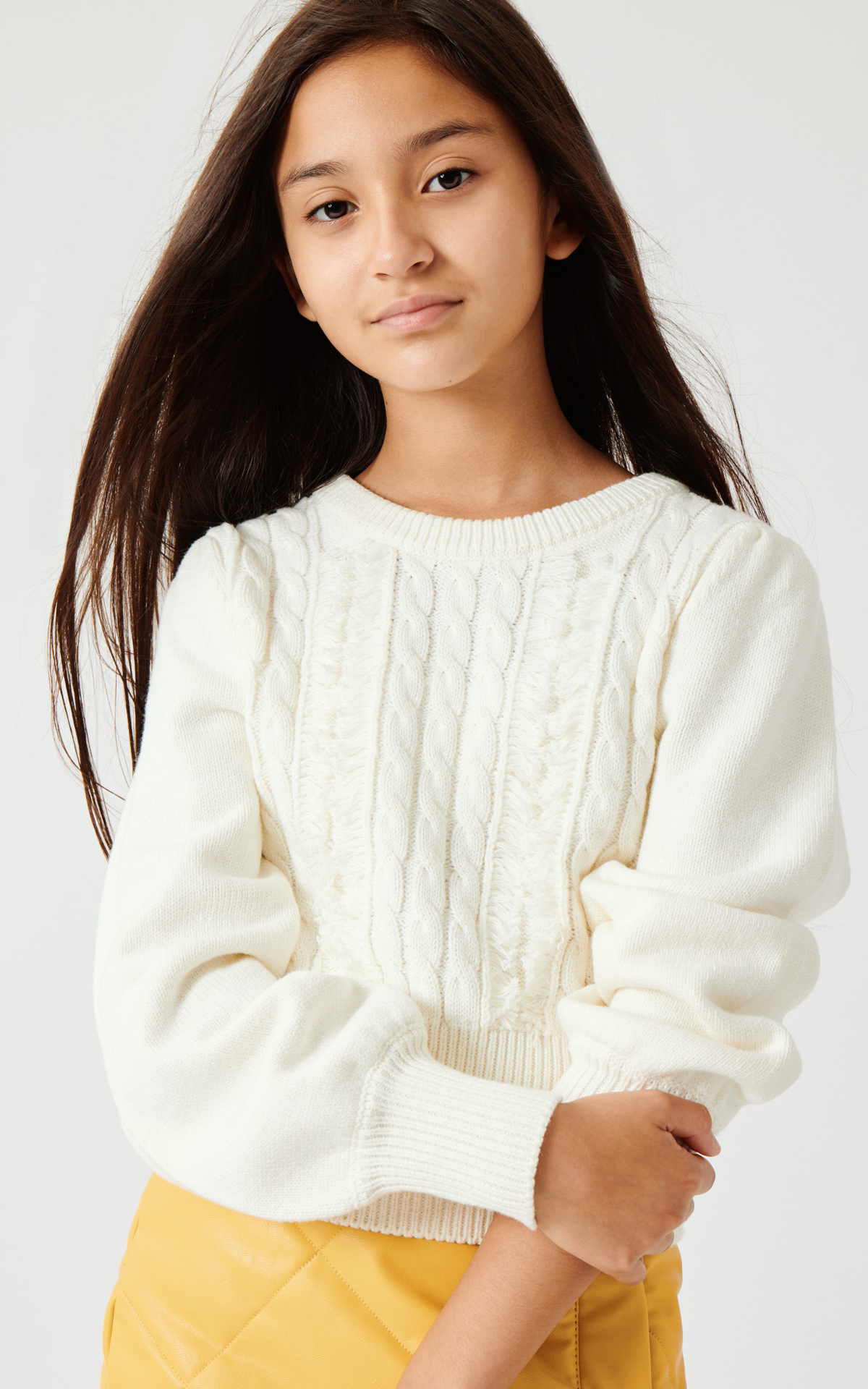 Tween girl wearing an off-white cable knit sweater and a yellow quilted skirt